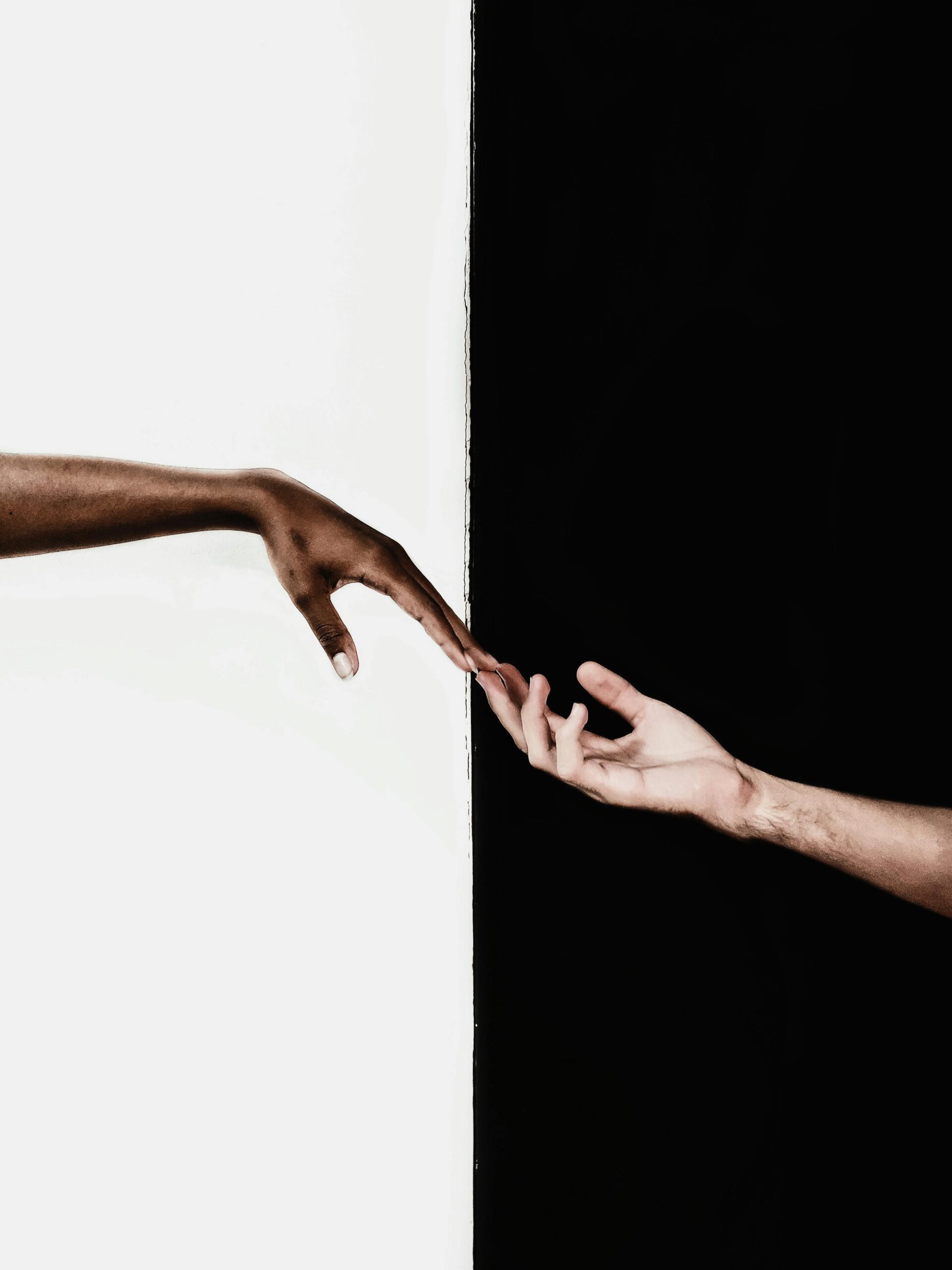 A black hand touching a white hand with opposite black and white backgrounds.